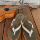 Paire de tongs en cuir MOOREA de couleur verte déposée sur des planches à côté d'une guitare