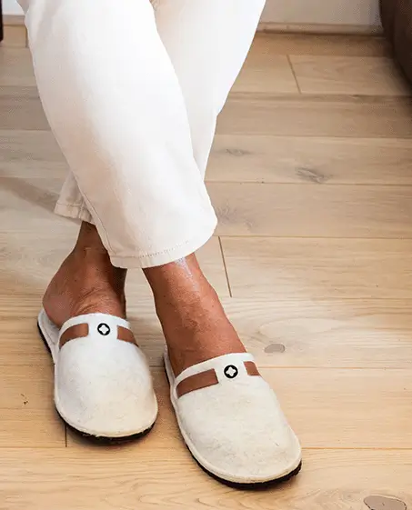 Bas des jambes d'un homme chic portant des chaussons en feutre de laine blanche portés avec un pantalon blanc sur un parquet en bois